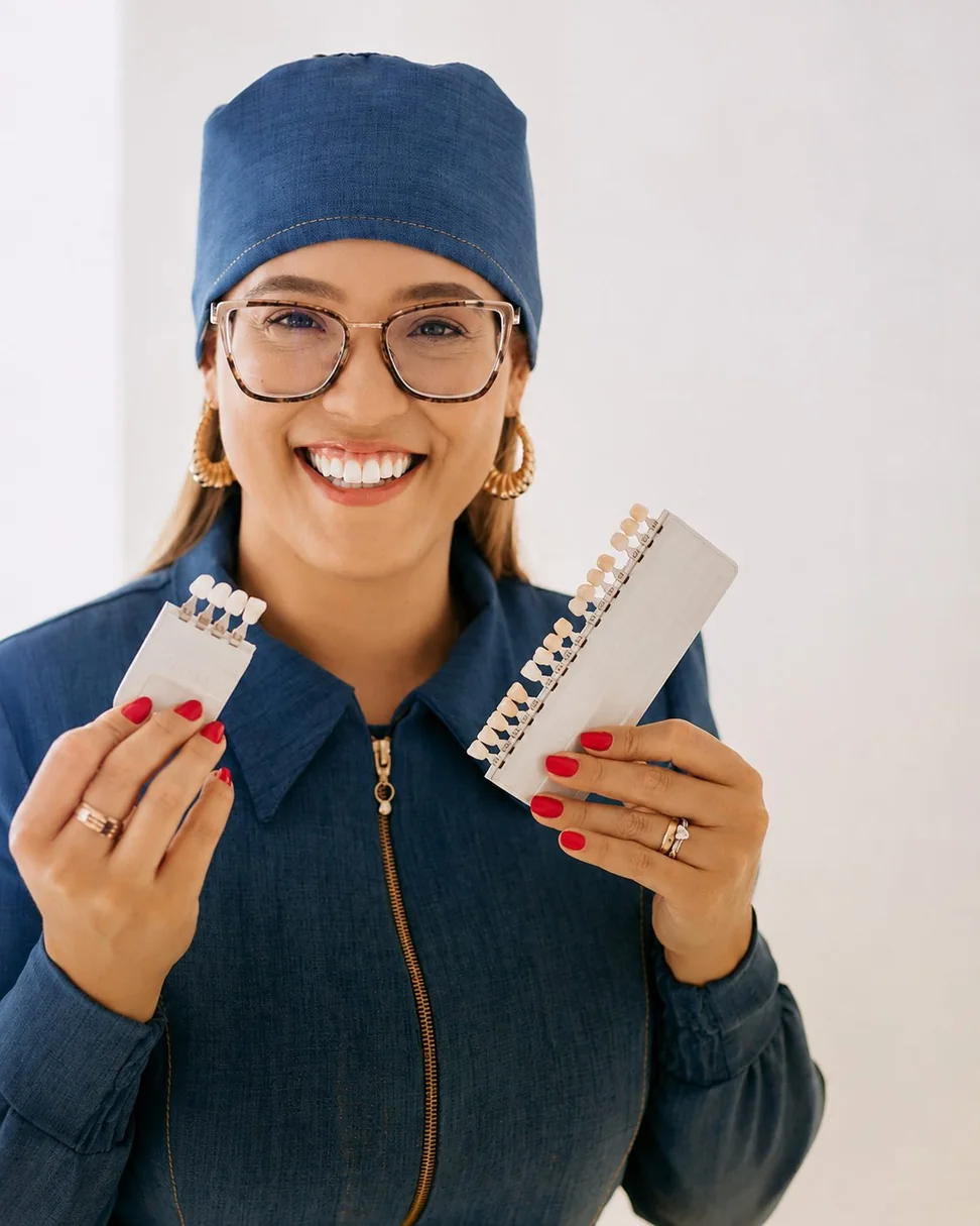 Dra. Deisielly Calaça sorrindo e segurando uma escala de cores dentais